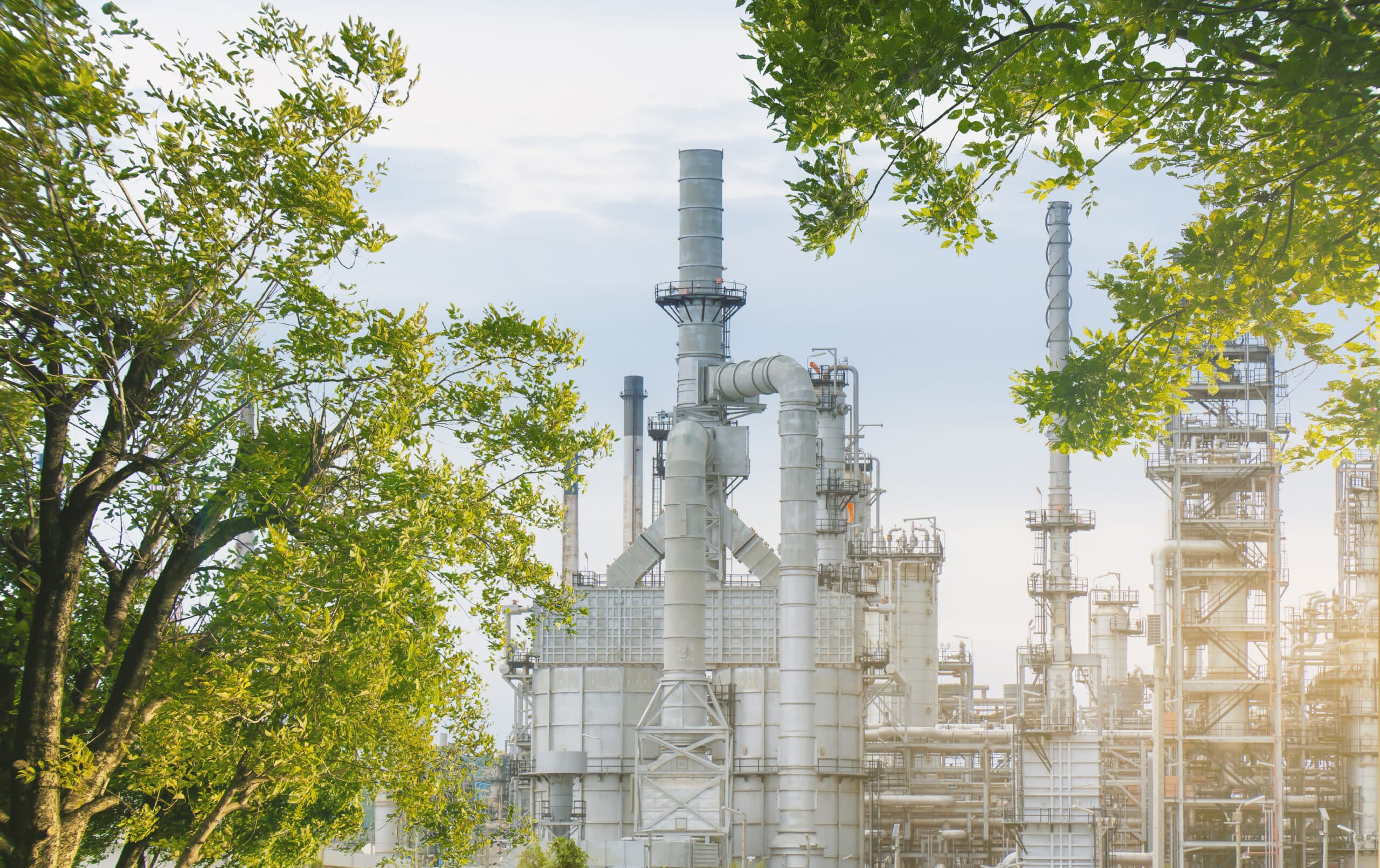Oil refinery plant from industry zone with tree and blue sky, large Oil and gas petrochemical industrial, Refinery factory oil storage tank and pipeline steel, Ecosystem and good environment.